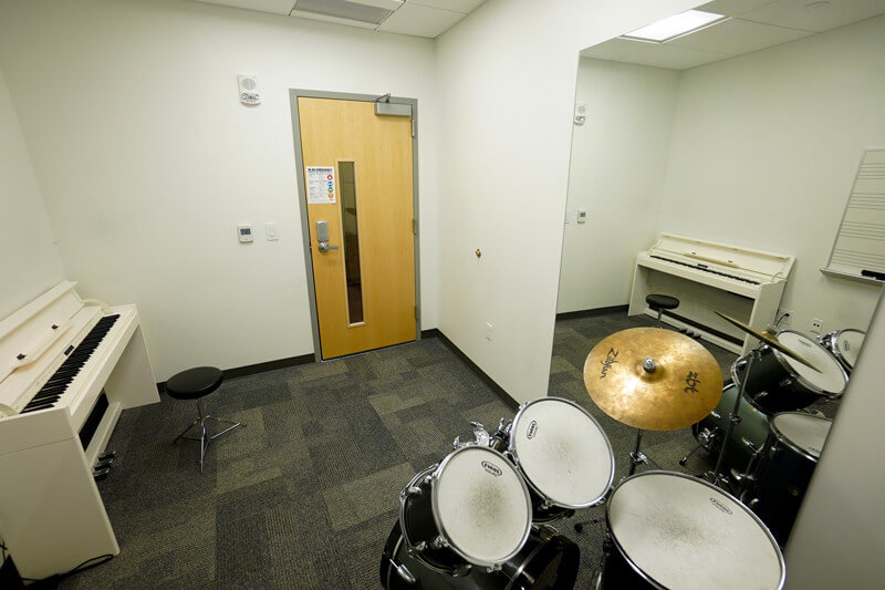 Practice room with piano, drum set, and mirror