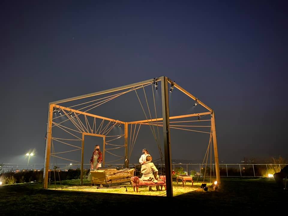 people on open-air stage with couch and cage