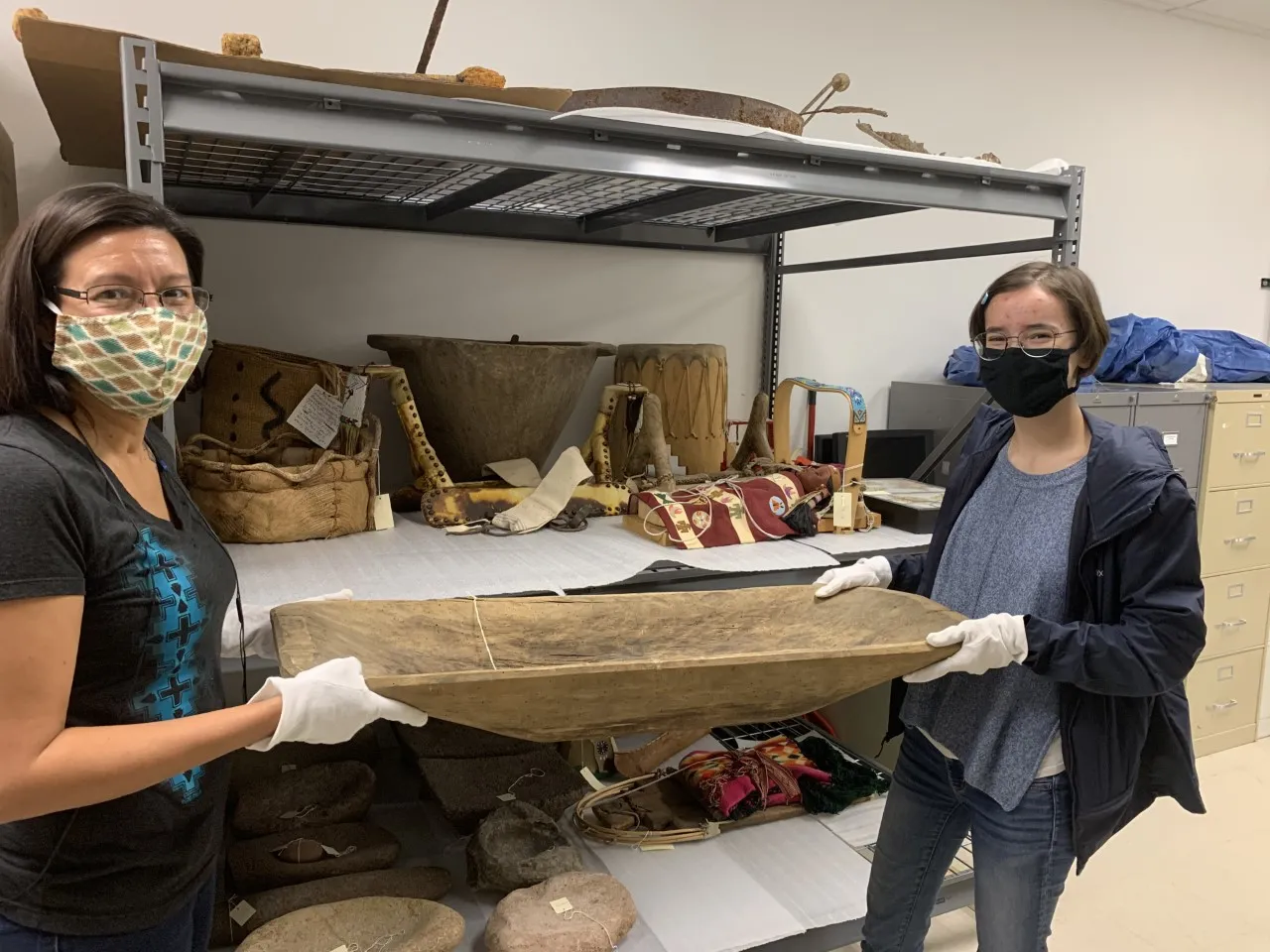 two people in masks holding Native American artifact