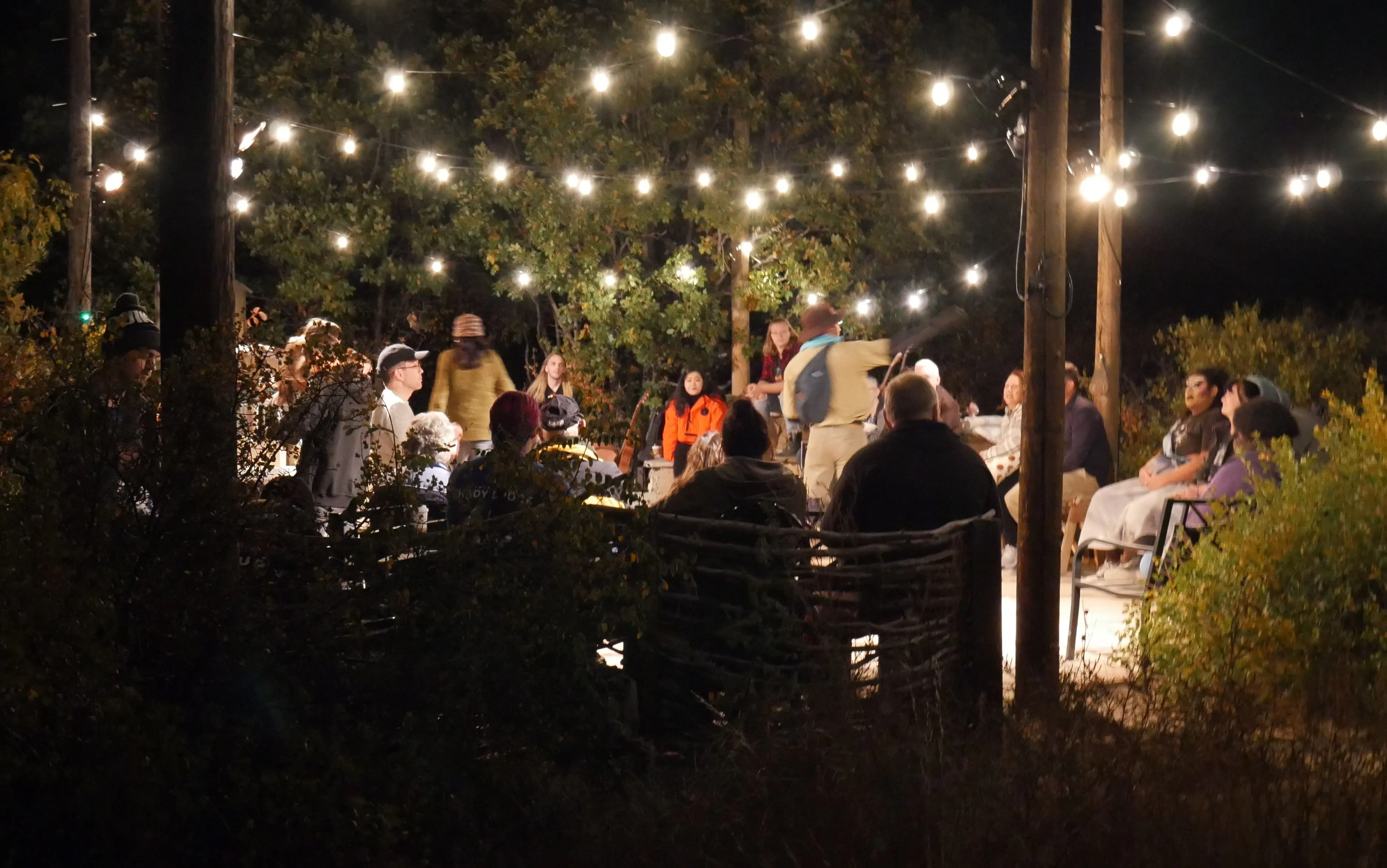 people on outdoor patio under strings of light telling stories