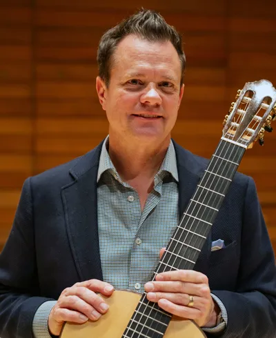 Colin Mcallister in navy suit holding an acoustic guitar