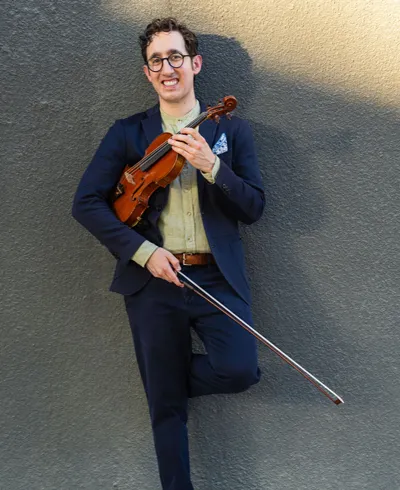 Michael DiBarry holding a violin and leaning against a wall